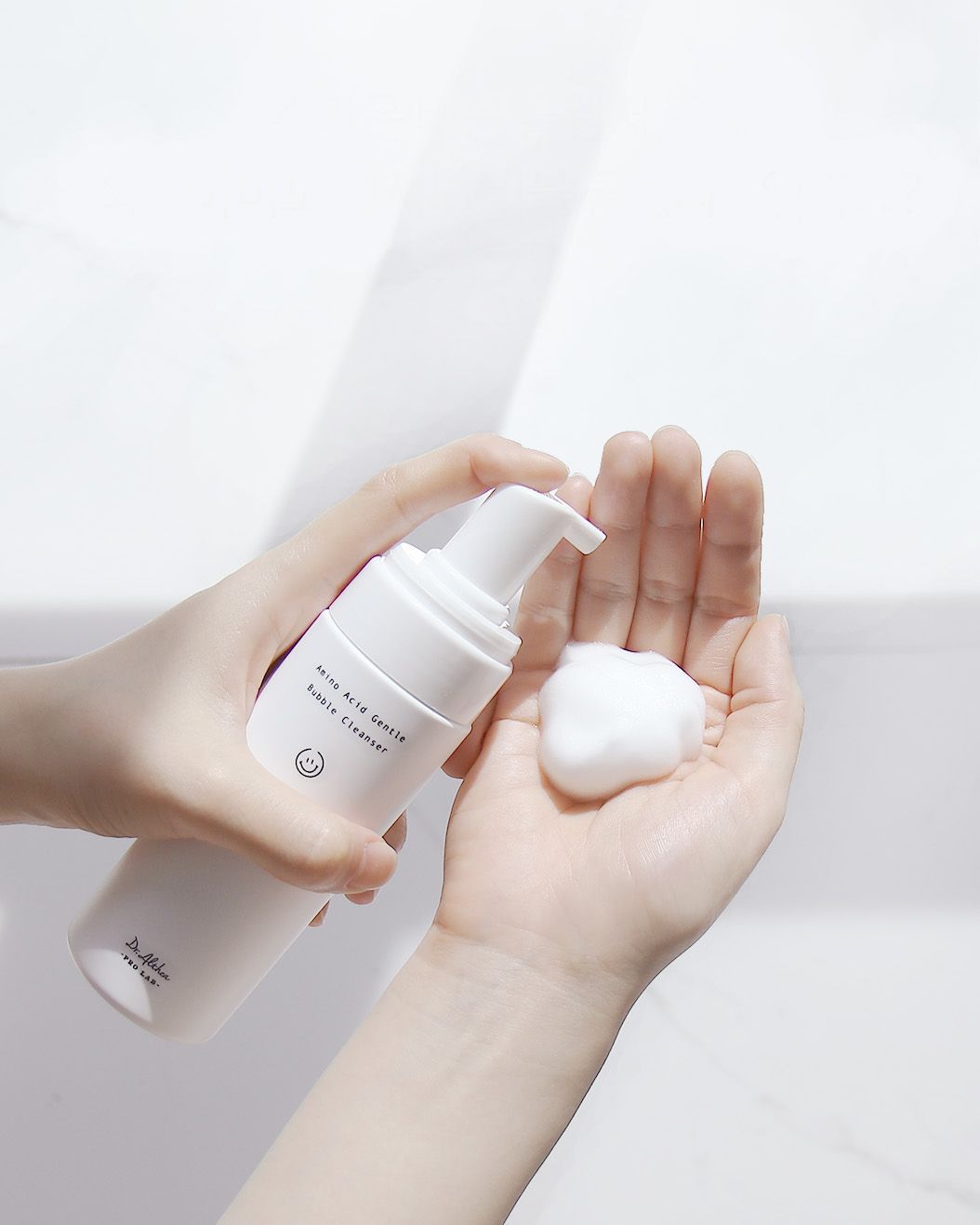 Person holding a white bottle with a pump dispenser on a light gray background